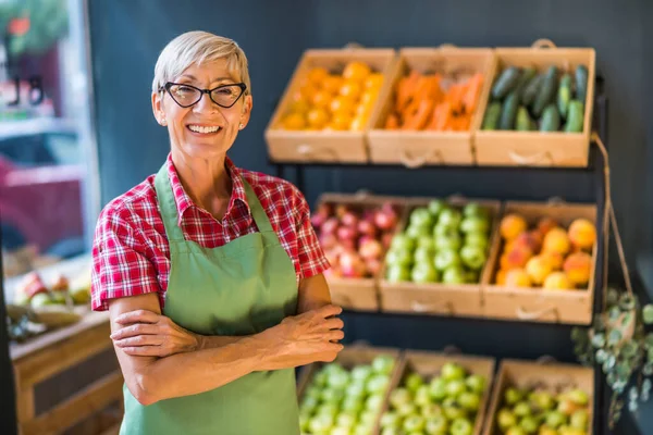 Mature woman works in fruits and vegetables shop. Portrait of small business supermarket owner.
