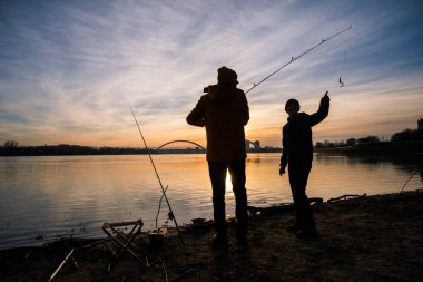 Father and son are fishing on winter day. River fishing. Teenage boy is learning to fish.