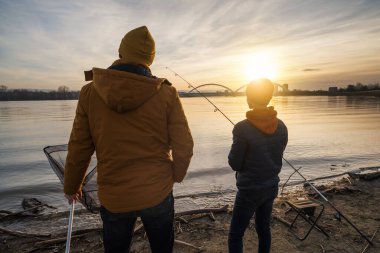Father and son are fishing on winter day. River fishing.