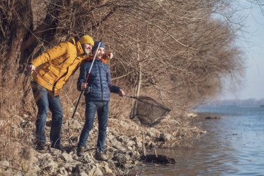 Father and son are fishing on sunny winter day. Freshwater fishing. Teenage boy is learning to fish.