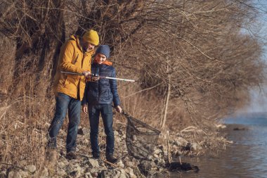 Father and son are fishing on sunny winter day. Freshwater fishing. Teenage boy is learning to fish.