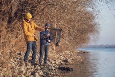 Father and son are fishing on sunny winter day. They caught a fish and are holding it in a landing net.