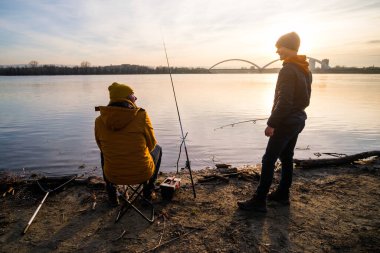 Father and son are fishing on winter day. River fishing. Teenage boy is learning to fish.