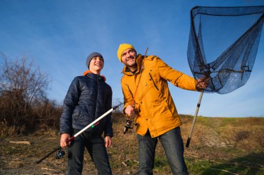 Father and son are fishing on sunny winter day. Freshwater fishing. Teenage boy is learning to fish.