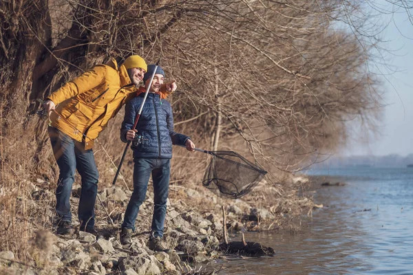 Father and son are fishing on sunny winter day. Freshwater fishing. Teenage boy is learning to fish.