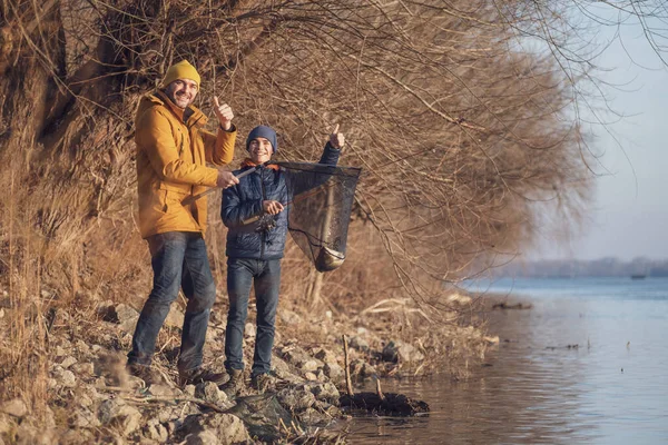 Father and son are fishing on sunny winter day. They caught a fish and are holding it in a landing net.