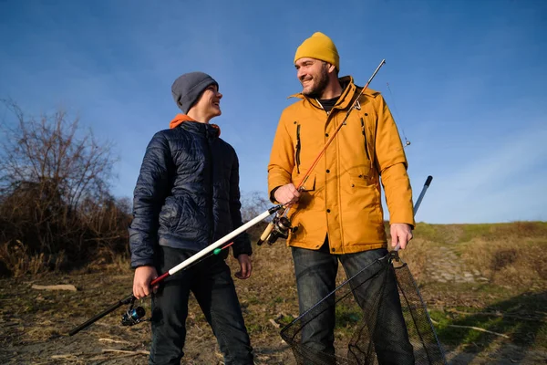 Father and son are fishing on sunny winter day. Freshwater fishing. Teenage boy is learning to fish.
