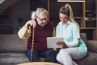 Nurse home caregiver is assisting old man at his home. Professional health support for elderly people.