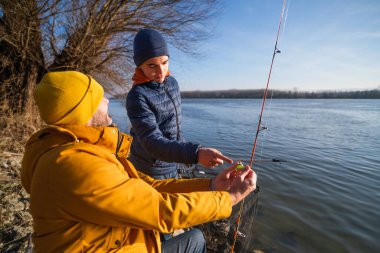 Father and son are fishing on sunny winter day. Freshwater fishing. Teenage boy is learning to fish.