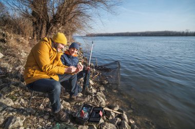 Father and son are fishing on sunny winter day. Freshwater fishing. Teenage boy is learning to fish.