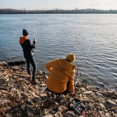 Father and son are fishing on sunny winter day. Freshwater fishing. Teenage boy is learning to fish.