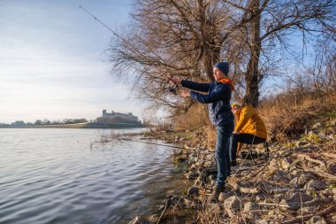 Father and son are fishing on sunny winter day. Freshwater fishing. Teenage boy is learning to fish.