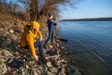 Father and son are fishing on sunny winter day. Freshwater fishing. Teenage boy is learning to fish.