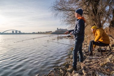 Father and son are fishing on sunny winter day. Freshwater fishing. Teenage boy is learning to fish.