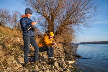 Father and son are fishing on sunny winter day. They caught a fish and are holding it in a landing net.