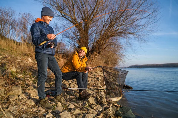 Father and son are fishing on sunny winter day. They caught a fish and are holding it in a landing net.