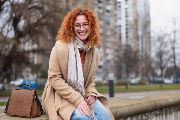 Natural portrait of a caucasian ginger woman with freckles and curly hair. She is smiling and looking at camera