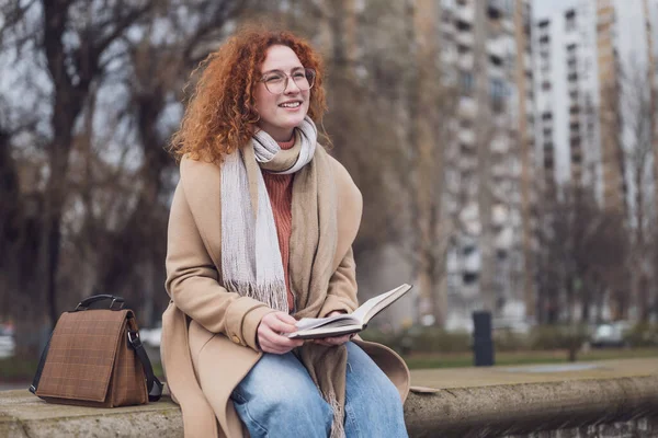 Natural portrait of a caucasian ginger woman with freckles and curly hair. She is reading book.