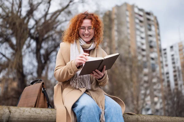 Natural portrait of a caucasian ginger woman with freckles and curly hair. She is reading book.