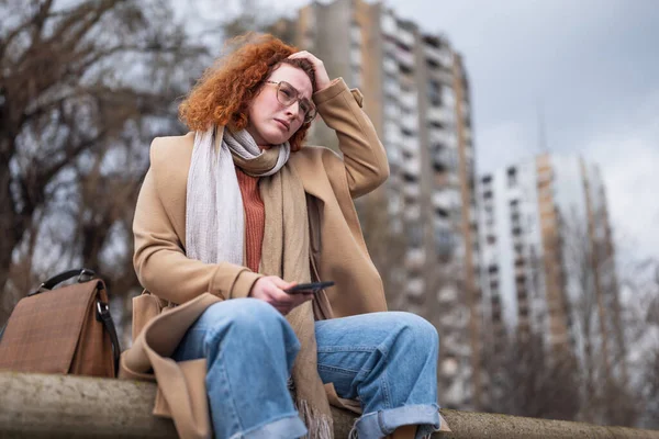 Natural portrait of a caucasian ginger woman with freckles and curly hair. She is depressed.
