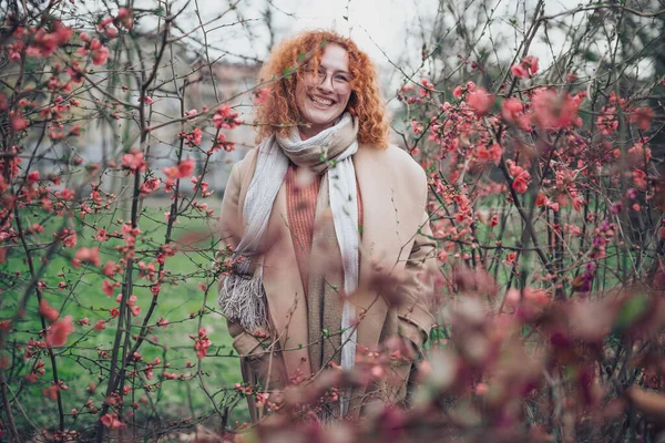 Natural portrait of a caucasian ginger woman with freckles and curly hair. She is smiling and looking away.