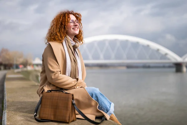 Natural portrait of a caucasian ginger woman with freckles and curly hair. She is smiling and enjoying sun.