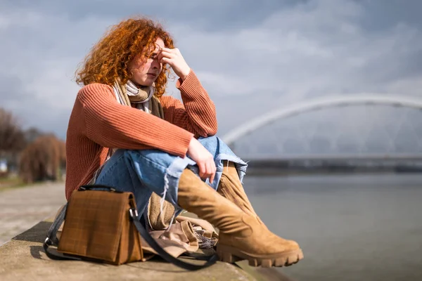 Natural portrait of a caucasian ginger woman with freckles and curly hair. She is tired and depressed.