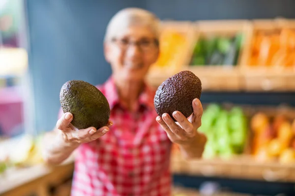 Worker in fruits and vegetables shop is holding avocado. Close up of avocado.