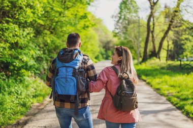 Güneşli bir günde doğa yürüyüşü yapan mutlu bir çift. El ele tutuşup yolda yürüyen bir çift..
