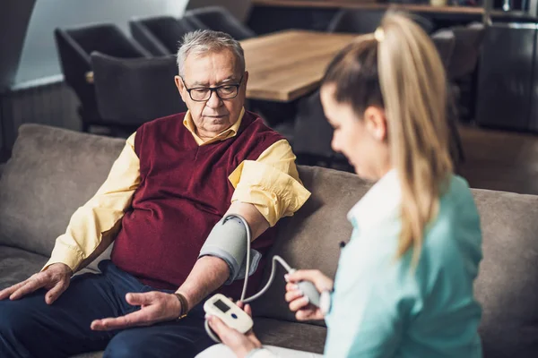 stock image Home doctor is measuring blood pressure of old man at his home. Professional health support for elderly people.