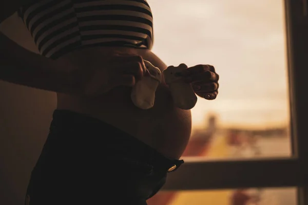 Mujer Embarazada Parada Junto Ventana Sosteniendo Calcetines Bebé Silueta Del —  Fotos de Stock
