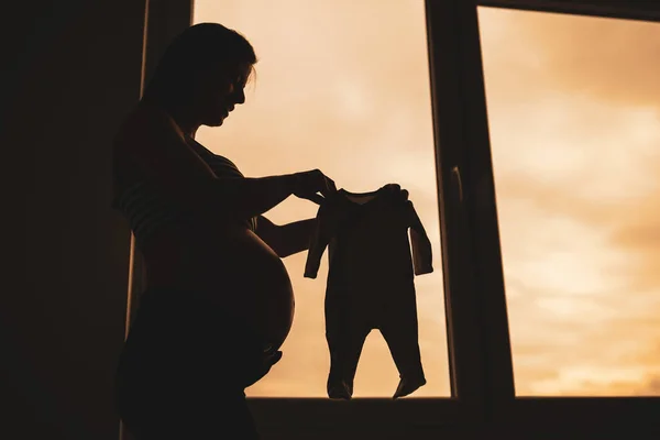 Gravid Kvinna Står Bredvid Fönstret Och Håller Baby Kläder Silhuett — Stockfoto