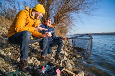 Father and son are fishing on sunny winter day. Freshwater fishing. Teenage boy is learning to fish.