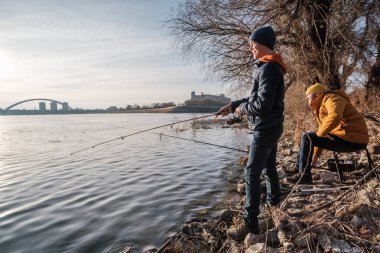 Father and son are fishing on sunny winter day. Freshwater fishing. Teenage boy is learning to fish.
