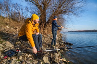 Father and son are fishing on sunny winter day. Freshwater fishing. Teenage boy is learning to fish.