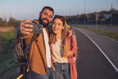 Mutlu gülümseyen çift günbatımının tadını çıkarıyor. Selfie çekiyorlar..