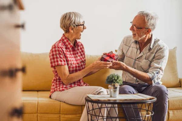 stock image Mature couple sitting in living room and celebrating their anniversary. Husband is giving present to his wife.