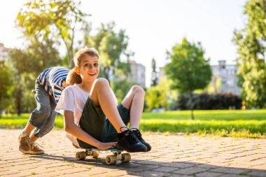 İki çocuk parkta kaykayla eğleniyor. Parkta neşeli çocuklar, mutlu bir çocukluk..