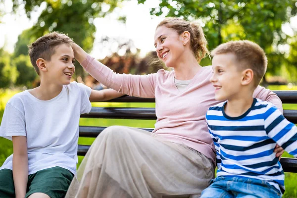 幸せな母親は公園で息子たちとベンチに座っている 彼らは話していると一緒に時間を楽しんでいる — ストック写真