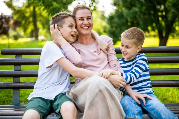 幸せな母親は公園で息子たちとベンチに座っている 彼らは一緒に楽しんでる — ストック写真