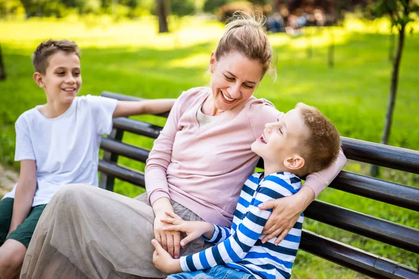 幸せな母親は公園で息子たちとベンチに座っている 彼らは一緒に楽しんでる — ストック写真