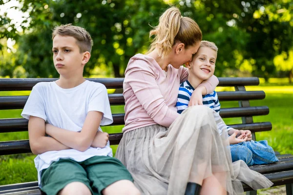 幸せな母親は公園で息子たちとベンチに座っている 一人の少年が怒って — ストック写真