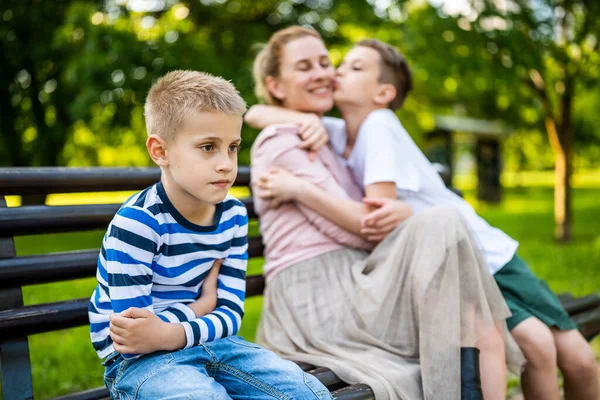 幸せな母親は公園で息子たちとベンチに座っている 一人の少年が怒って — ストック写真