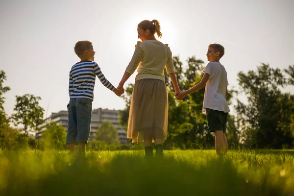 幸せな母親は公園で息子たちと遊んでいる 手を取り合いながら夕日を楽しんでいます — ストック写真