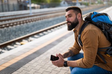Yetişkin adam tren istasyonunda oturuyor ve trenin gelişini bekliyor..