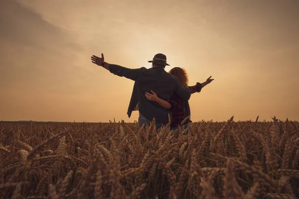 幸せな男と女は日没時に彼らの農地に立っている 小麦を栽培し 良い農業の季節を楽しんでいます — ストック写真