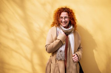 Gülümseyen, kızıl saçlı, çilli, kıvırcık saçlı bir kadının doğal portresi..