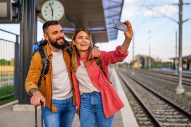 Mutlu çift tren istasyonunda duruyor ve trenlerinin gelmesini bekliyor. Selfie çekiyorlar..