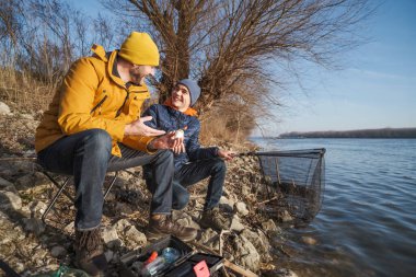 Father and son are fishing on sunny winter day. Freshwater fishing. Teenage boy is learning to fish.