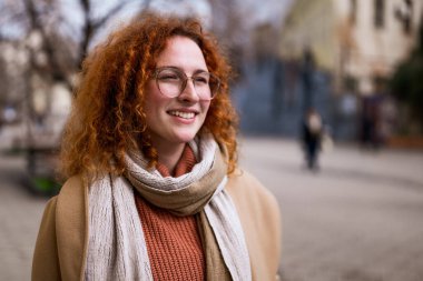 Gülümseyen, kızıl saçlı, çilli, kıvırcık saçlı bir kadının doğal portresi..